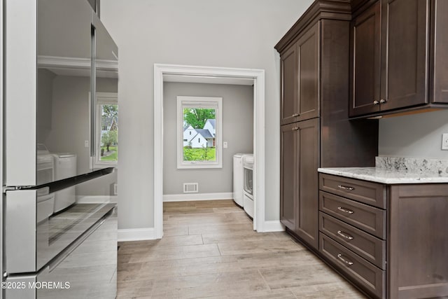 clothes washing area featuring independent washer and dryer, light wood finished floors, and baseboards