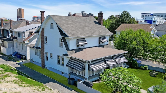 back of house featuring a chimney, a shingled roof, and a lawn