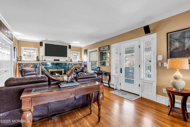 living room with wood-type flooring, a premium fireplace, crown molding, baseboard heating, and baseboards