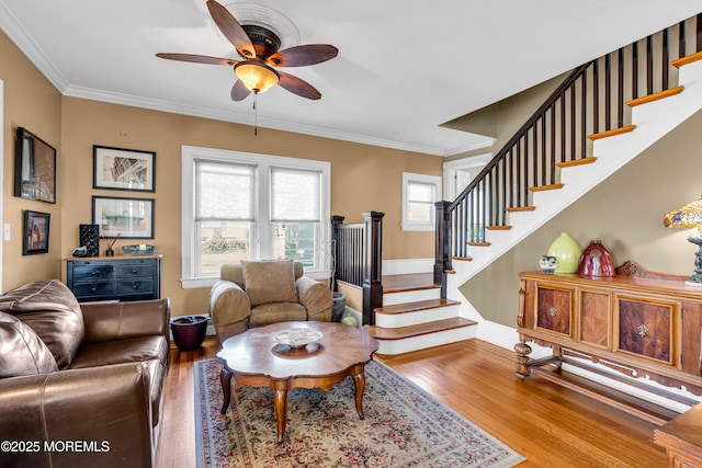 living room with wood finished floors, ceiling fan, stairs, baseboards, and crown molding
