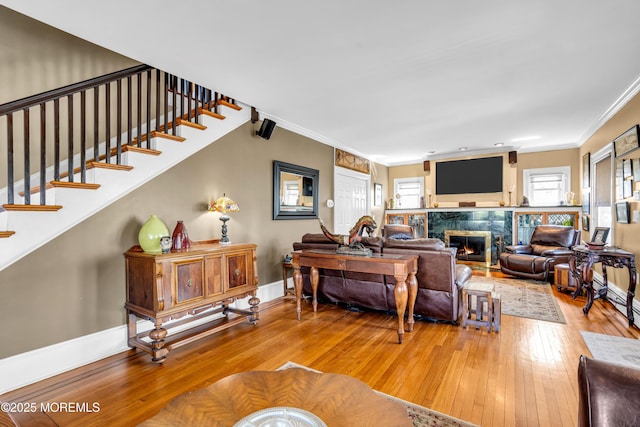 living room with stairway, baseboards, hardwood / wood-style flooring, crown molding, and a tiled fireplace