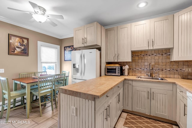 kitchen featuring white fridge with ice dispenser, a sink, ornamental molding, a ceiling fan, and backsplash