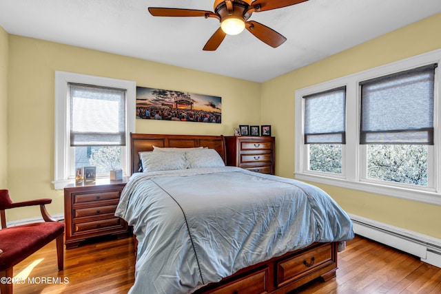 bedroom with wood finished floors, a ceiling fan, and a baseboard heating unit