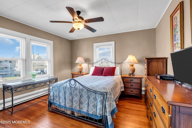 bedroom with hardwood / wood-style flooring, multiple windows, a baseboard heating unit, and crown molding