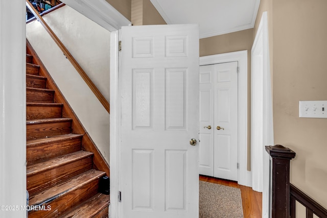 staircase with wood finished floors and ornamental molding