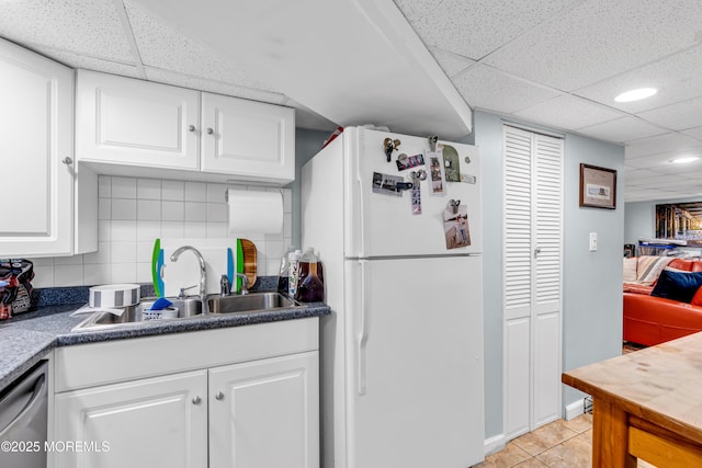 kitchen featuring freestanding refrigerator, a drop ceiling, a sink, stainless steel dishwasher, and white cabinetry