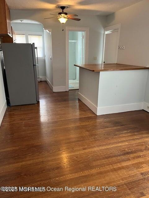 kitchen with freestanding refrigerator, baseboards, ceiling fan, dark wood-type flooring, and arched walkways