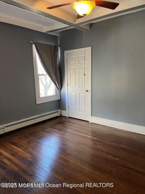 unfurnished bedroom with a baseboard heating unit, wood finished floors, beam ceiling, baseboards, and a ceiling fan