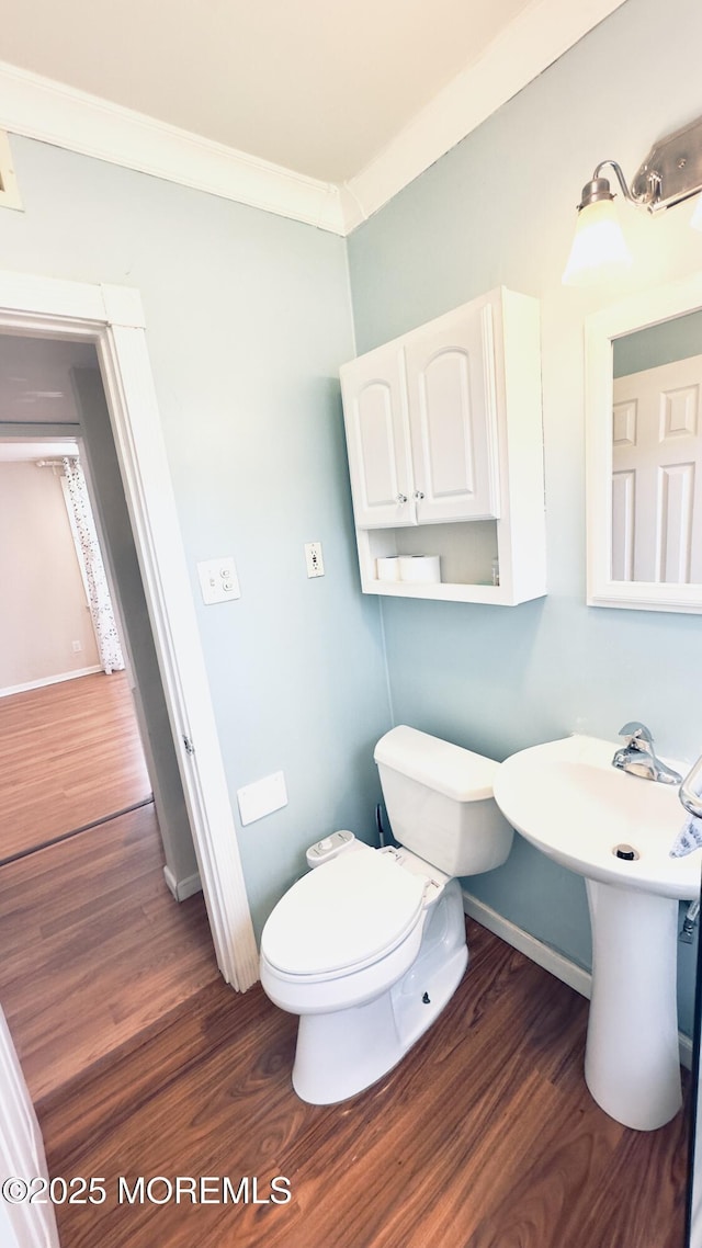 half bathroom with baseboards, wood finished floors, toilet, and crown molding