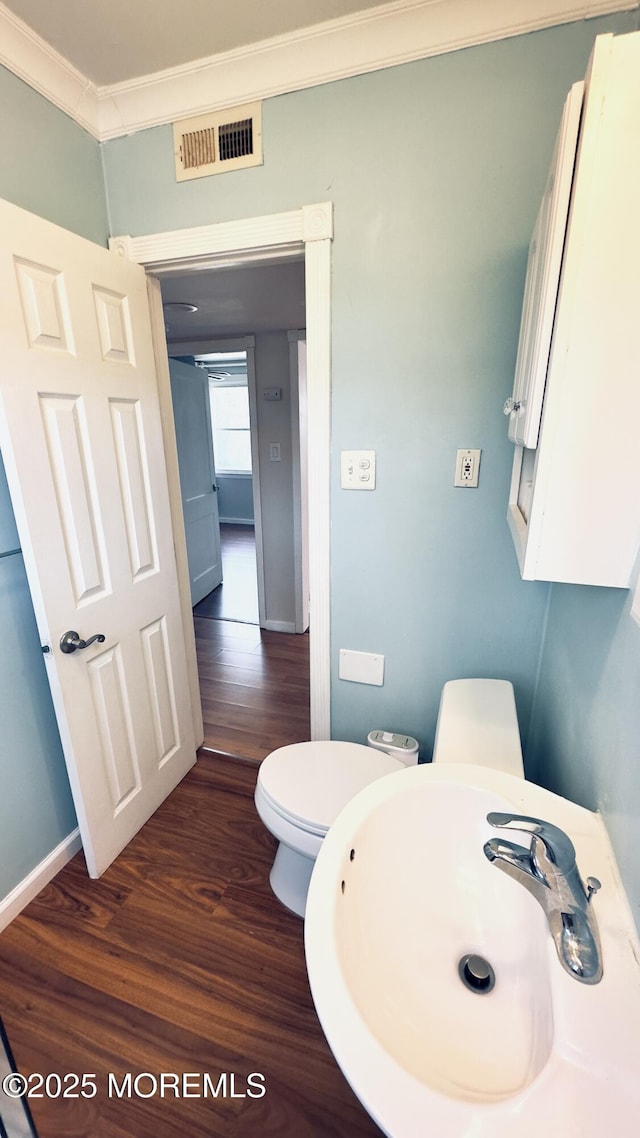 bathroom with a sink, crown molding, wood finished floors, toilet, and baseboards