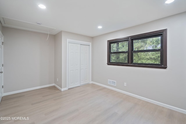 unfurnished bedroom featuring attic access, light wood-type flooring, baseboards, recessed lighting, and a closet