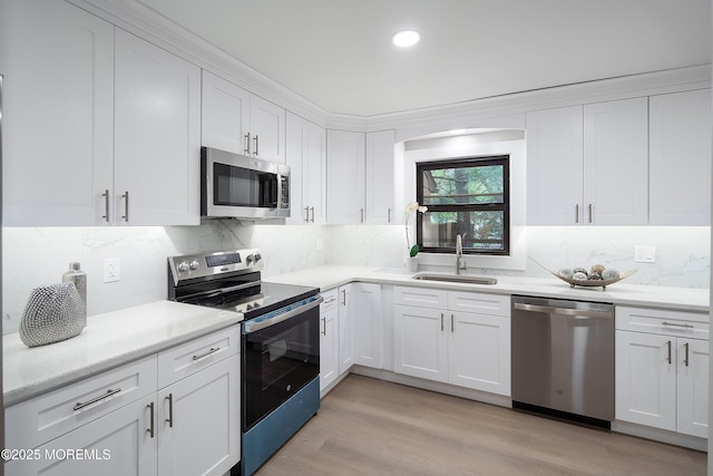 kitchen featuring stainless steel appliances, a sink, white cabinetry, tasteful backsplash, and light wood-style floors
