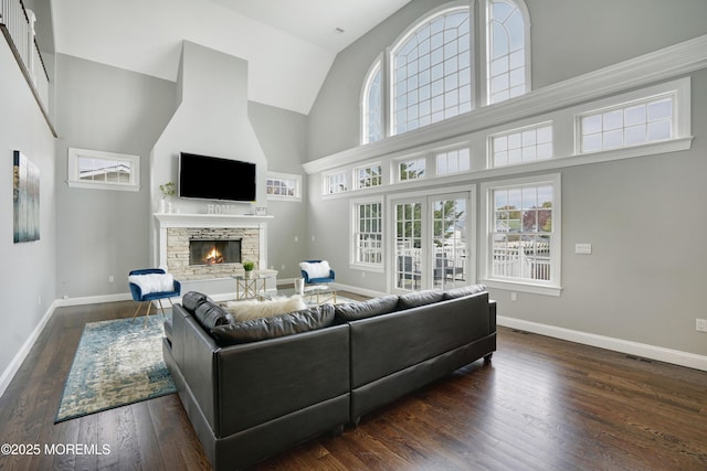 living room featuring high vaulted ceiling, a fireplace, baseboards, wood finished floors, and healthy amount of natural light