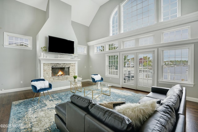 living area featuring high vaulted ceiling, a fireplace, baseboards, and wood finished floors