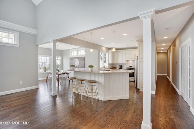 kitchen with stainless steel range oven, decorative columns, a breakfast bar area, plenty of natural light, and recessed lighting