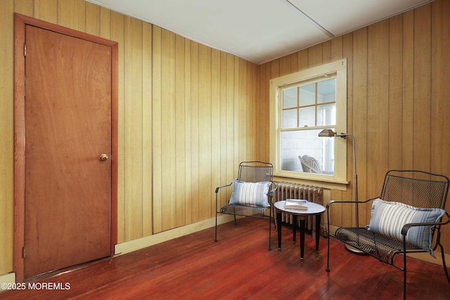 sitting room with wood finished floors, wood walls, and radiator heating unit