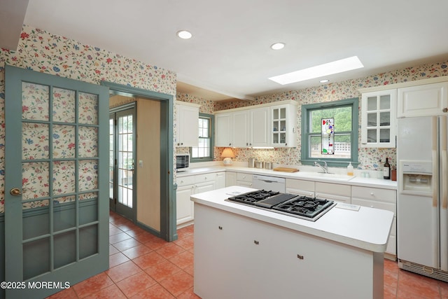 kitchen with white appliances, a skylight, a sink, wallpapered walls, and light tile patterned flooring