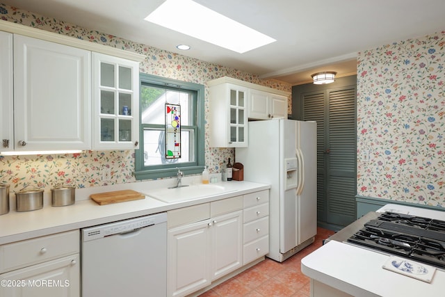 kitchen with white appliances, wallpapered walls, a sink, white cabinets, and glass insert cabinets