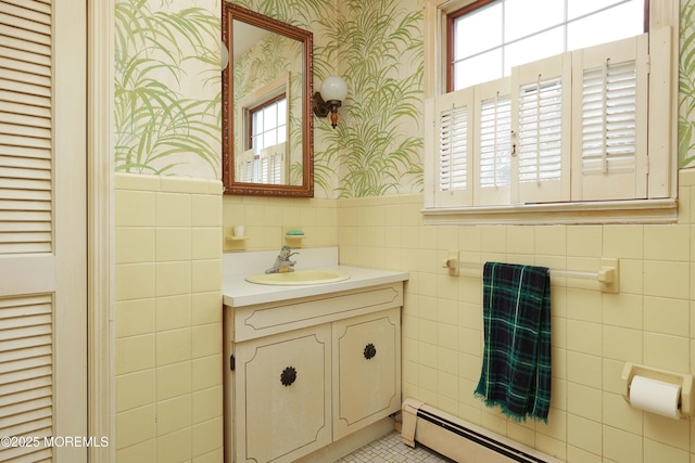 bathroom with wallpapered walls, tile walls, baseboard heating, wainscoting, and vanity