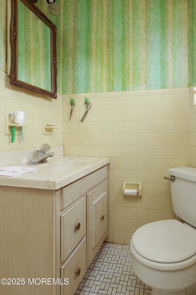 half bath with tile walls, toilet, and vanity