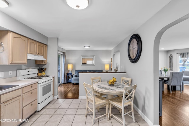 2124 3rd Ave, Toms River, NJ 08757 - kitchen featuring white range with gas cooktop, under cabinet range hood, light brown cabinets, arched walkways, and baseboards