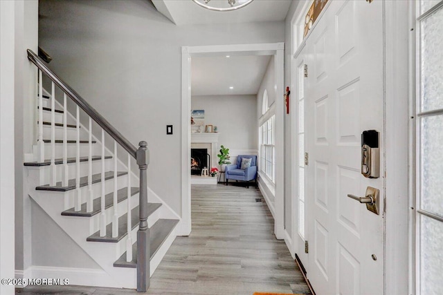foyer featuring a lit fireplace, stairway, wood finished floors, baseboards, and recessed lighting