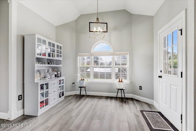 foyer with a chandelier, light wood-type flooring, healthy amount of natural light, high vaulted ceiling, and baseboards