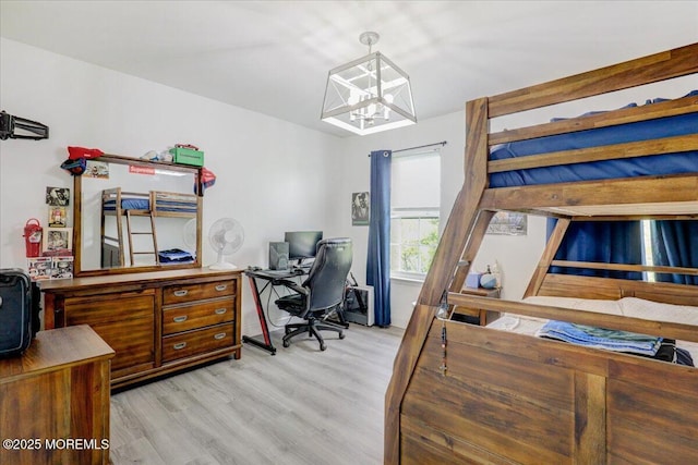 bedroom with an office area, light wood-style floors, and a chandelier