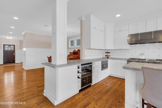 3 Sunset Dr, Asbury Park, NJ 07712 - kitchen with wine cooler, under cabinet range hood, stainless steel microwave, white cabinets, and crown molding