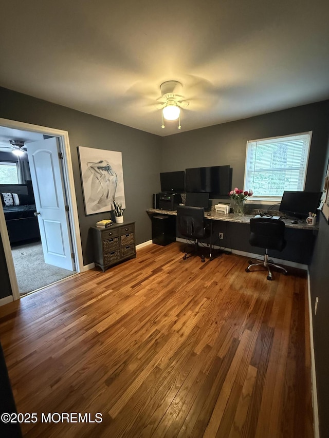 office space featuring ceiling fan, wood finished floors, and built in desk