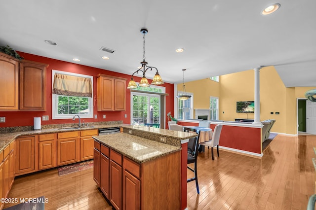 kitchen featuring a sink, a breakfast bar, a kitchen island, pendant lighting, and light wood-style flooring