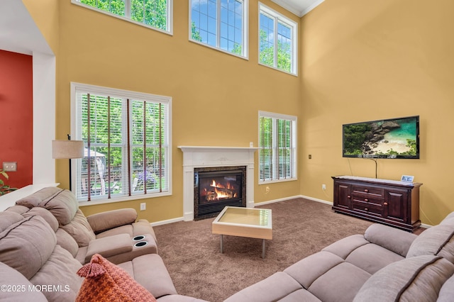 carpeted living area featuring healthy amount of natural light, a high ceiling, a high end fireplace, baseboards, and crown molding