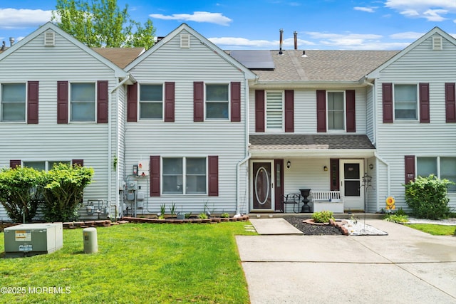 view of property with a porch, a front yard, roof with shingles, and roof mounted solar panels