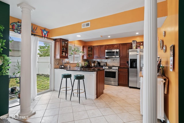 kitchen featuring ornate columns, stainless steel appliances, a peninsula, dark countertops, and backsplash
