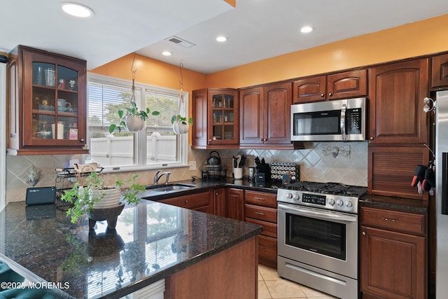 kitchen featuring stainless steel appliances, a sink, a peninsula, glass insert cabinets, and dark stone countertops