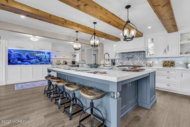kitchen featuring white cabinetry, wood finished floors, tasteful backsplash, light countertops, and beamed ceiling