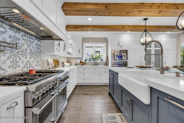 kitchen with double oven range, wall chimney range hood, a sink, white cabinetry, and beam ceiling