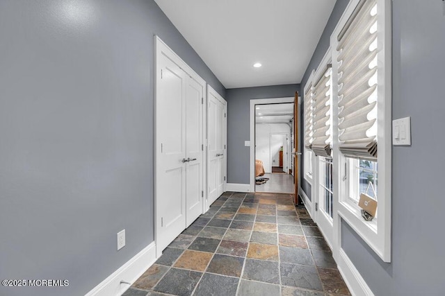 hall with stone tile flooring, baseboards, and recessed lighting
