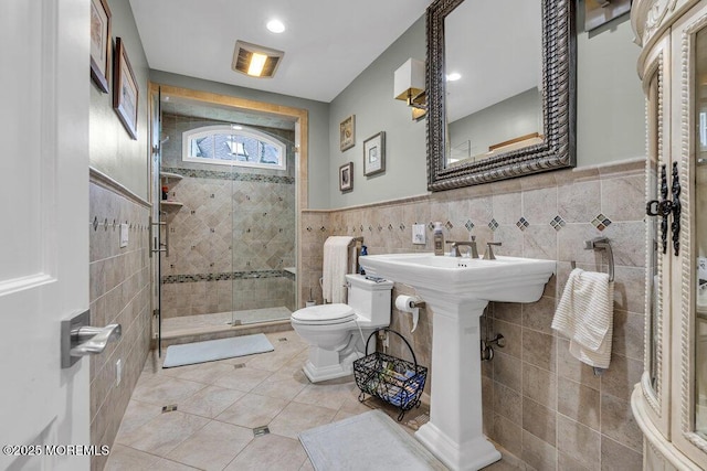 full bath featuring tile walls, toilet, a stall shower, tile patterned flooring, and a wainscoted wall