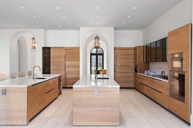 27 N Ward Ave, Rumson, NJ 07760 - kitchen with a large island with sink, modern cabinets, a sink, light tile patterned floors, and arched walkways