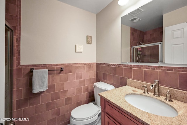 full bathroom with tile walls, a shower stall, toilet, vanity, and a wainscoted wall