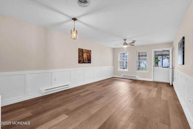 28 Mill Rd Unit B, Whiting, NJ 08759 - unfurnished room featuring a baseboard radiator, ceiling fan, a wainscoted wall, wood finished floors, and a decorative wall