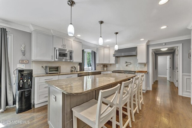 25 Briar Hill Dr, Manalapan, NJ 07726 - kitchen featuring wall chimney exhaust hood, stainless steel appliances, tasteful backsplash, a breakfast bar, and light stone countertops