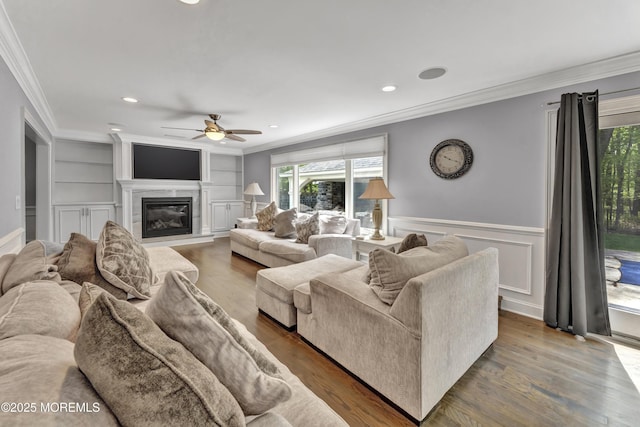 25 Briar Hill Dr, Manalapan, NJ 07726 - living room with ornamental molding, ceiling fan, a glass covered fireplace, a wainscoted wall, and built in shelves