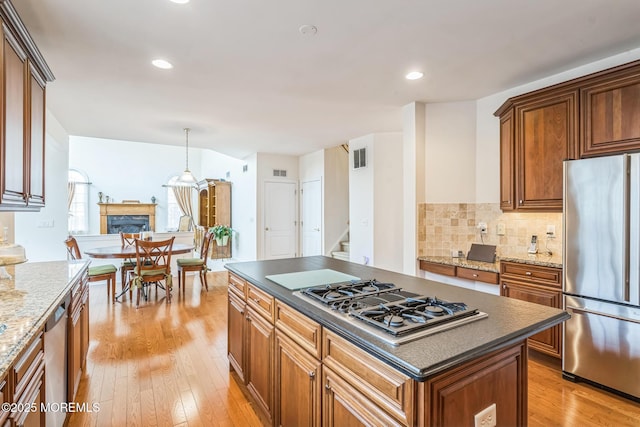 5 Duke Dr, Howell, NJ 07731 - kitchen with appliances with stainless steel finishes, a fireplace, light wood-type flooring, brown cabinetry, and decorative backsplash