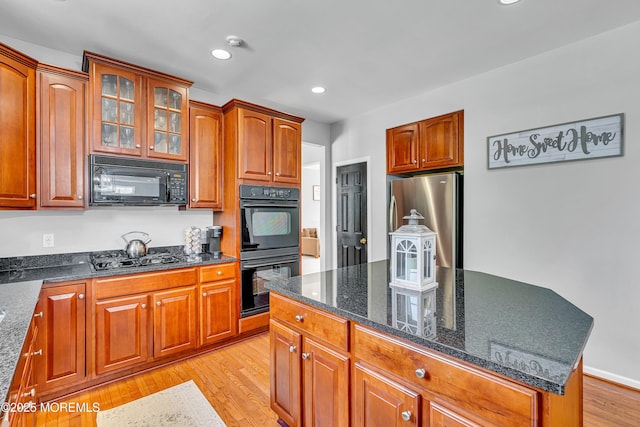 707 Cedar Point Ct, Toms River, NJ 08753 - kitchen with black appliances, light wood-style flooring, dark stone countertops, glass insert cabinets, and a kitchen island