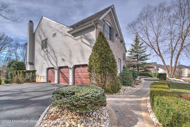 11 Elkridge Way, Manalapan, NJ 07726 - view of side of property featuring driveway, a chimney, and a garage