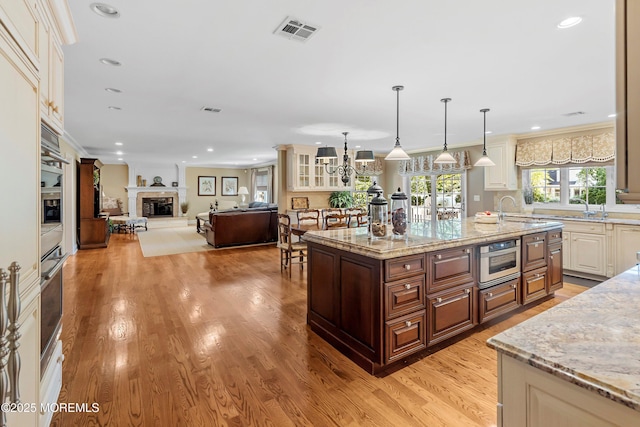 10 Woods Rd, West Long Branch, NJ 07764 - kitchen featuring a glass covered fireplace, a sink, light wood-type flooring, light stone countertops, and a kitchen island with sink
