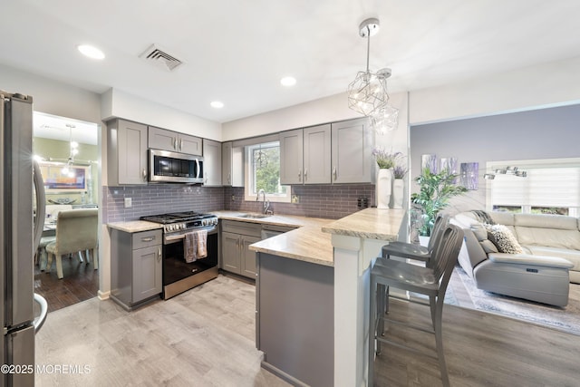 9 Crossridge Cir, Marlboro, NJ 07746 - kitchen with gray cabinetry, stainless steel appliances, a peninsula, a breakfast bar, and light wood-type flooring