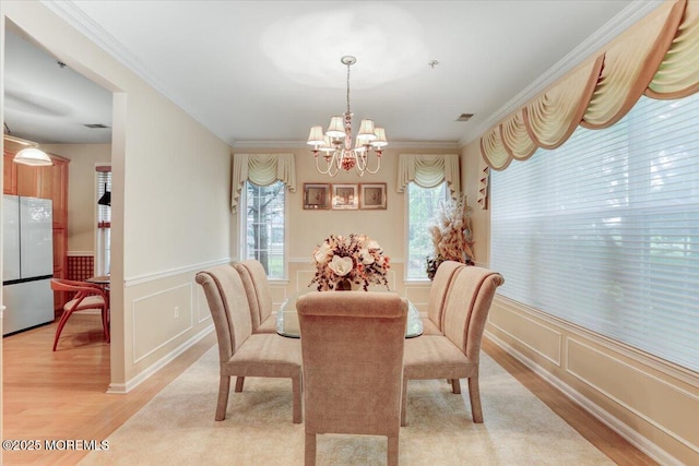 634 Saint Andrews Pl, Manalapan, NJ 07726 - dining area with a chandelier, light wood-style floors, crown molding, a decorative wall, and a wainscoted wall